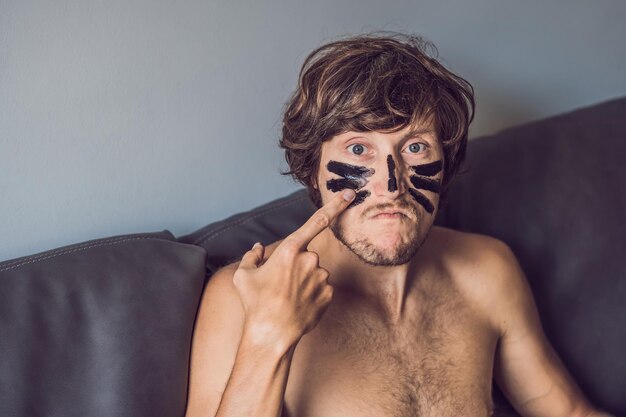 Hombre feliz con máscara negra en la cara. Foto hombre recibiendo tratamientos de spa. Concepto de cuidado de la piel de belleza