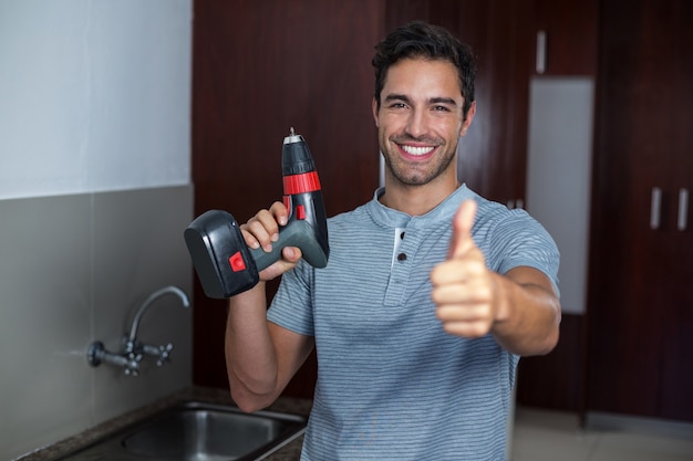 Hombre feliz mostrando los pulgares hacia arriba mientras sostiene el taladro de mano inalámbrico