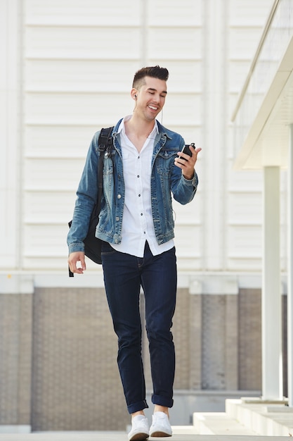 Hombre feliz con móvil y auriculares caminando afuera