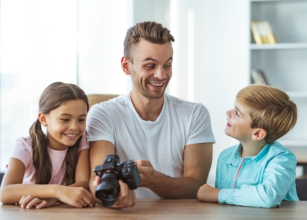 El hombre feliz con niños sosteniendo una cámara en la mesa.