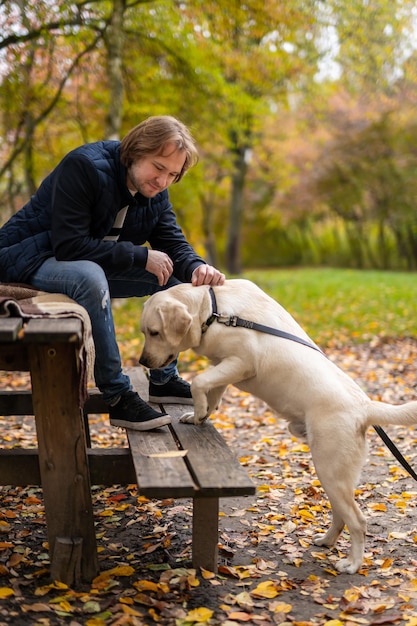 Hombre feliz con perro en el parque. Labrador huele un banco en el parque. Concepto de mejores amigos.