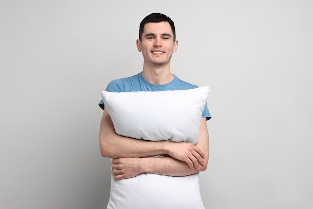 Hombre feliz en pijama sosteniendo una almohada sobre un fondo gris claro