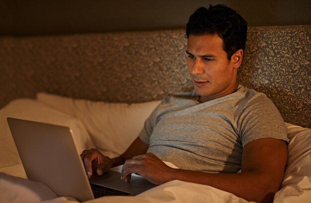 Hombre feliz y portátil en el dormitorio por la noche suscripción en línea y transmisión de películas para ver el fin de semana persona tranquila relajarse y computadora en la cama en el edredón bienestar y desplazarse en las redes sociales en el hogar