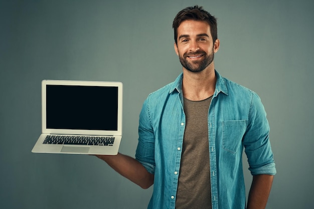 Foto hombre feliz portátil y pantalla de maqueta para publicidad o marketing contra un fondo de estudio gris retrato de una persona masculina con una sonrisa que muestra la pantalla de la computadora o un espacio de maqueta para publicidad