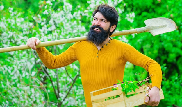 Hombre feliz preparándose para plantar agricultor con pala de jardinería y trabajo de somier de madera en el jardín