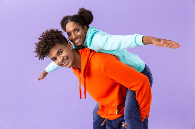 Hombre feliz que lleva a cuestas a su hermana joven, aislado sobre la pared violeta