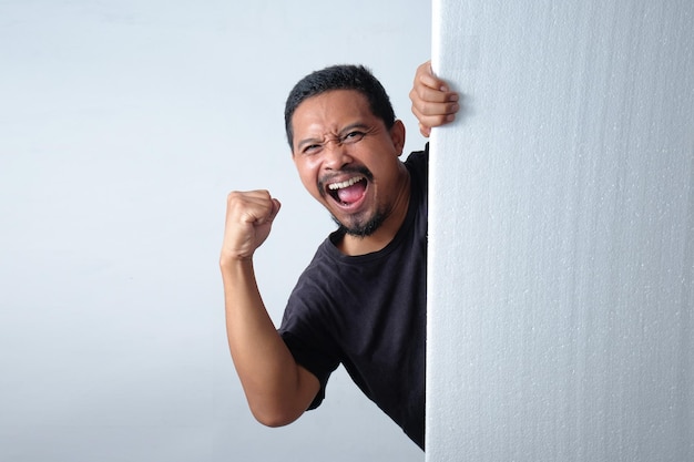 Hombre feliz que mira a escondidas detrás de la pared