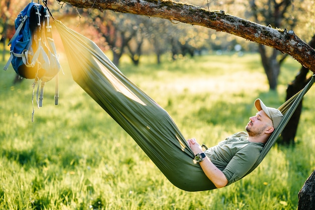 Hombre feliz que se relaja en la hamaca que cuelga en manzano en parque soleado del verano.