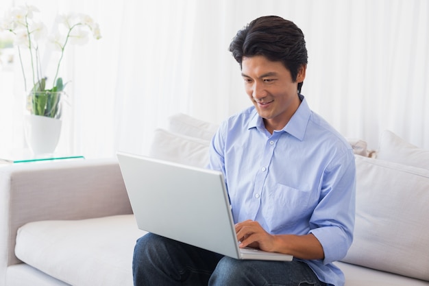 Hombre feliz que se sienta en el sofá usando la computadora portátil