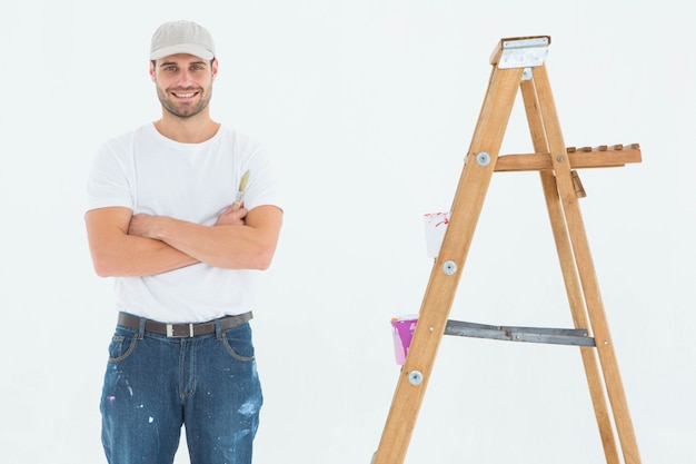 Hombre feliz que sostiene el rodillo de pintura mientras que está parado por la escalera