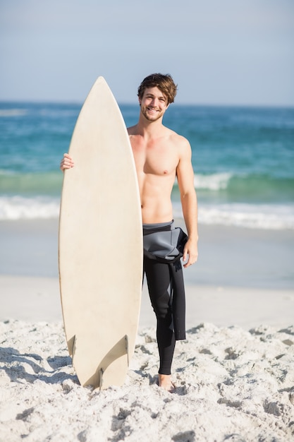 Hombre feliz que sostiene una tabla de surf en la playa