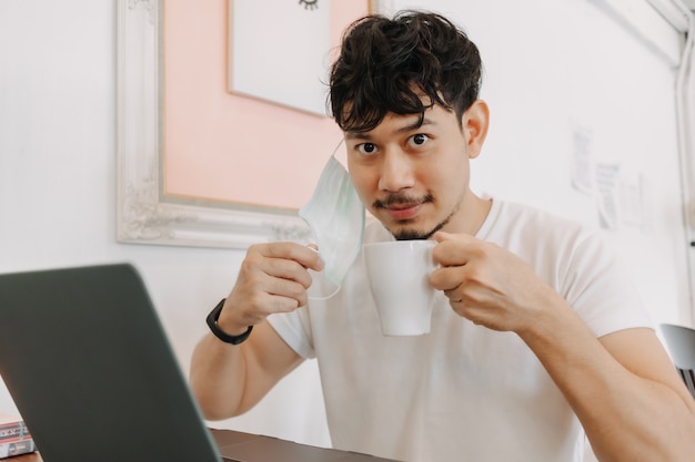 Hombre feliz quitándose la máscara para tomar café mientras trabajaba en la cafetería