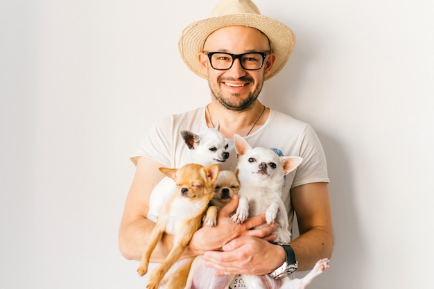 Hombre feliz riendo en sombrero de paja abraza a cuatro cachorros de chihuahua