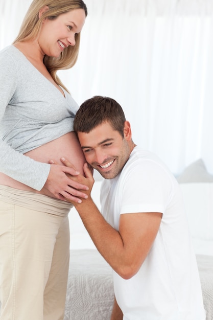 Hombre feliz en la rodilla escuchando el vientre de su esposa embarazada