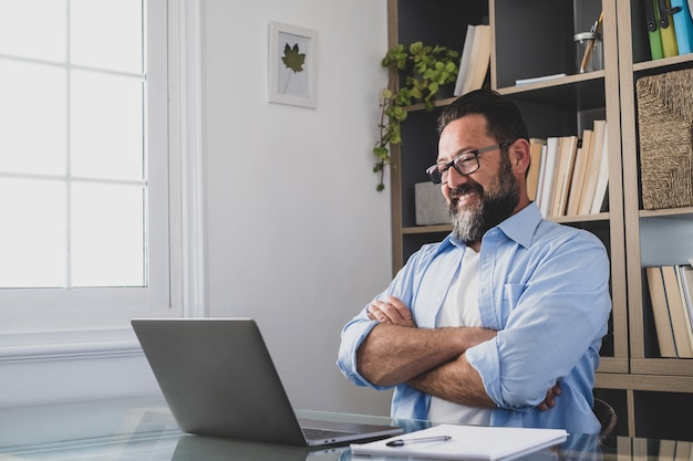 Un hombre feliz y satisfecho sonriendo y mirando su trabajo en la pantalla de la computadora. Gente masculina relajante después de terminar el trabajo en la oficina de la casa interior.