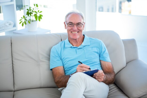 Hombre feliz senior en anteojos sentado en el sofá con portapapeles