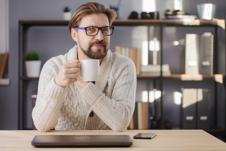 Hombre feliz sentado en la mesa con café y mirando a la cámara
