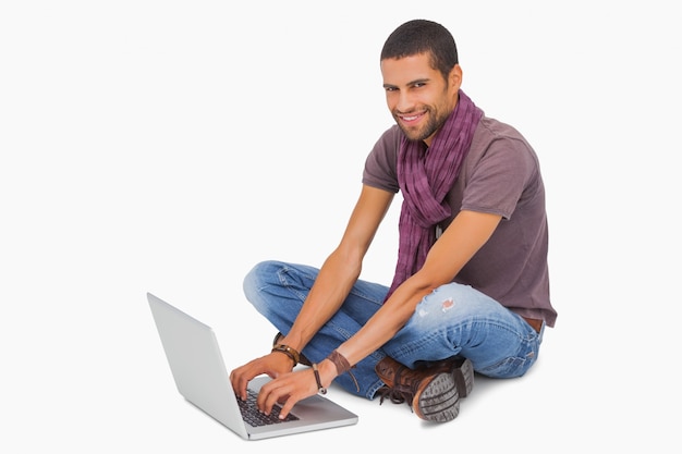 Hombre feliz sentado en el piso usando la computadora portátil