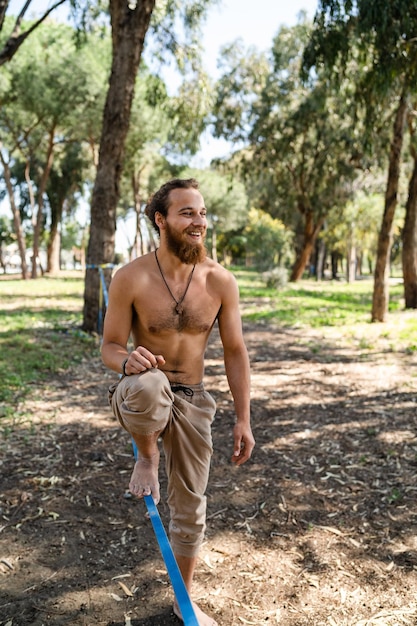 Hombre feliz slackline en el parque de la ciudad durante el día de verano