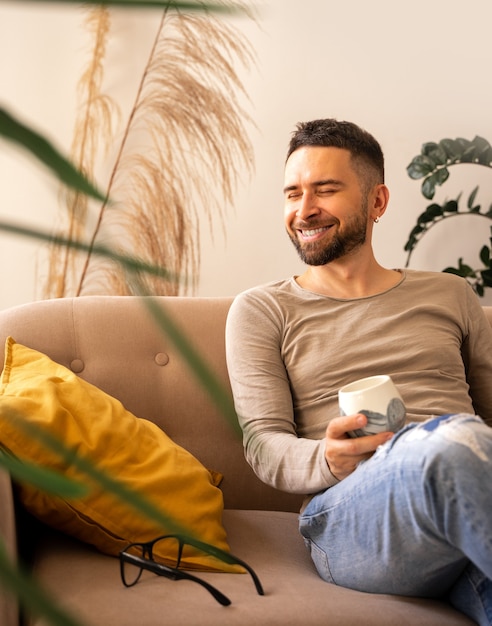 Foto hombre feliz sonriendo y descansando retrato de un hombre sentado en un sofá con almohada amarilla en casa con