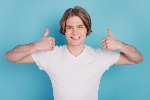Hombre feliz con sonrisa radiante mostrando dos manos pulgar arriba aislado sobre fondo azul.