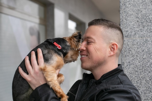 Hombre feliz sostener en las manos perrito y besar al bozal vista lateral hombre adulto sonriente caminar con mascota outd