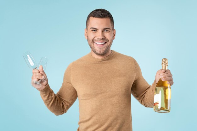 Hombre feliz sosteniendo copas y botella de champán sobre fondo azul.