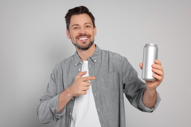 Hombre feliz sosteniendo lata con bebida sobre fondo gris claro