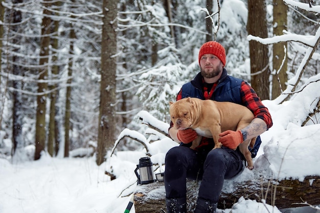 Hombre feliz sosteniendo un perro encantador en sus manos en un bosque nevado Niño sonriente abrazando a un adorable cachorro en madera de invierno Amante de las mascotas Concepto de amigo del perro humano