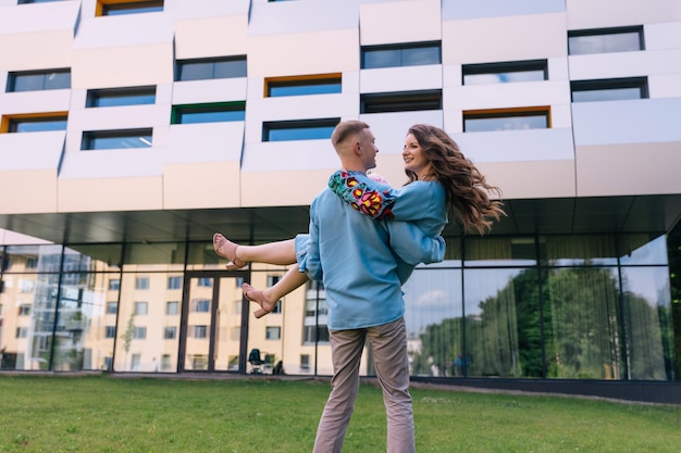 Foto un hombre feliz sostiene a una mujer en sus brazos y gira con ella en el fondo de un edificio