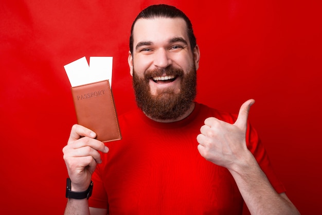 Un hombre feliz sostiene un pasaporte con dos boletos y muestra un pulgar hacia arriba