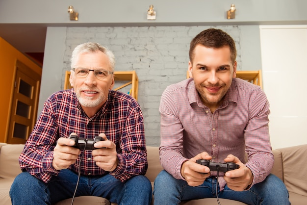 Foto hombre feliz y su padre jugando videojuegos mientras está sentado en el sofá