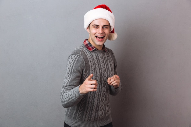 Hombre feliz en suéter y sombrero de navidad apuntando