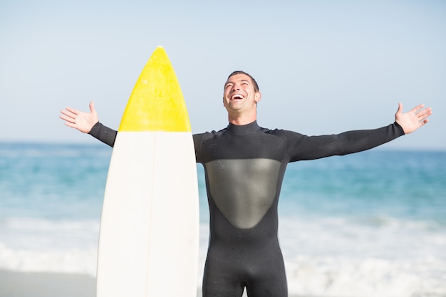 Hombre feliz con tabla de surf de pie en la playa