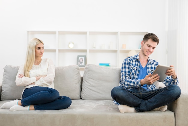 El hombre feliz con una tableta se sienta cerca de la mujer en el sofá