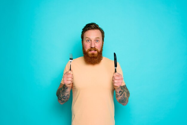 Hombre feliz con tatuajes está listo para comer con cubiertos en mano