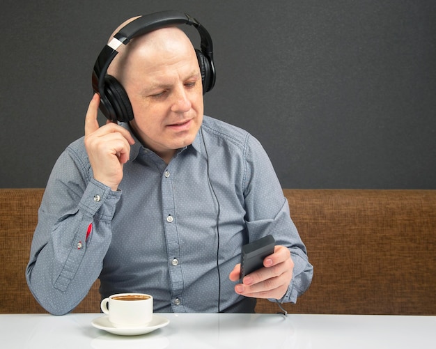 Hombre feliz con una taza de café en auriculares portátiles escucha música con un reproductor.