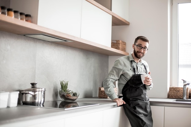 Hombre feliz con una taza de té de pie en la cocina