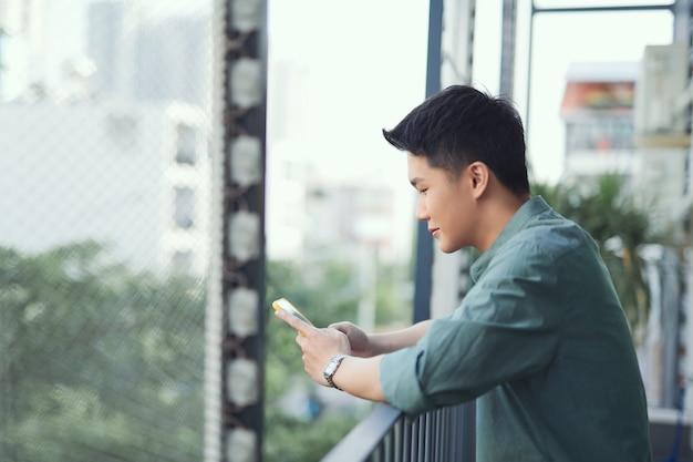 Hombre feliz con teléfono móvil en el balcón