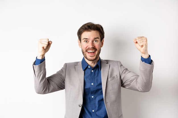 Hombre feliz en traje levantando las manos y cantando, viendo juegos deportivos, ganando en el casino y celebrando, de pie emocionado sobre fondo blanco.