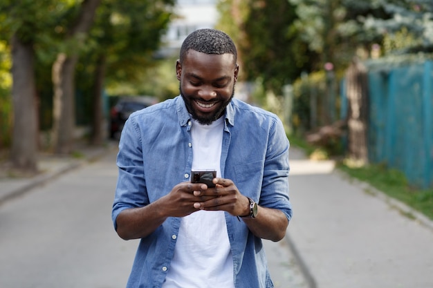 Hombre feliz usando aplicaciones de teléfono móvil, enviando mensajes de texto, navegando por internet, mirando el teléfono inteligente