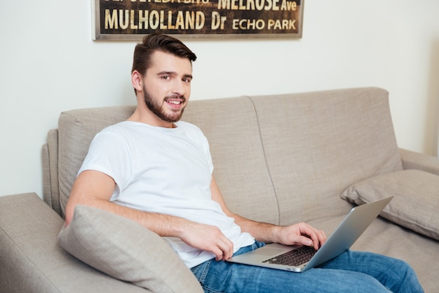 Hombre feliz usando la computadora portátil en el sofá en casa