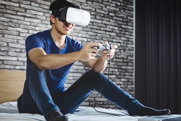 Foto hombre feliz usando un simulador de realidad virtual con un joystick en la cama en casa