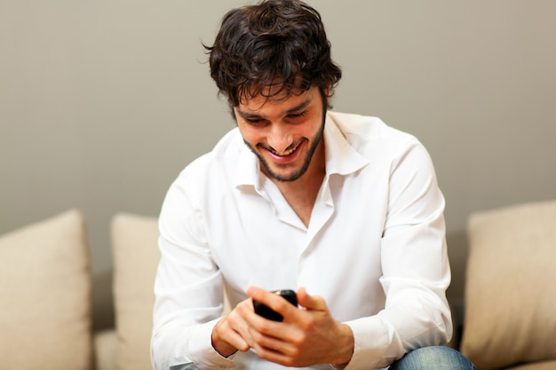 Hombre feliz usando su teléfono inteligente sentado en un sofá