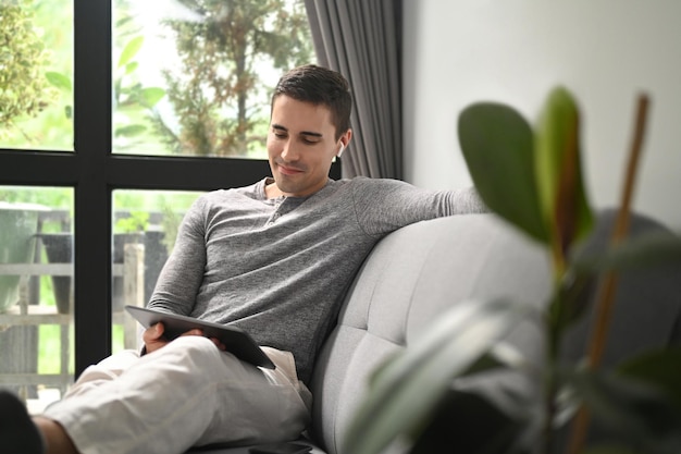 Hombre feliz usando tableta digital mientras se sienta en un cómodo sofá