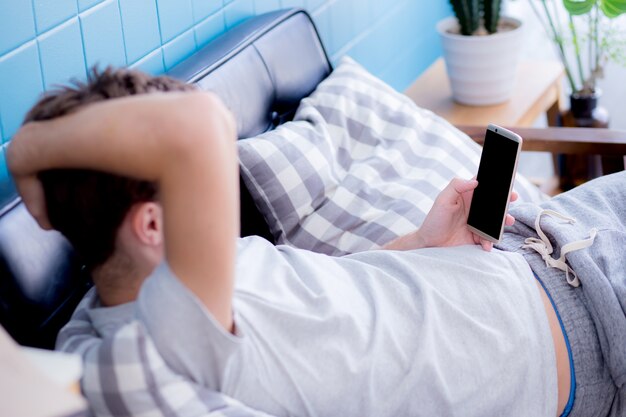 Hombre feliz viendo contenido multimedia en un móvil sentado en un sofá en casa