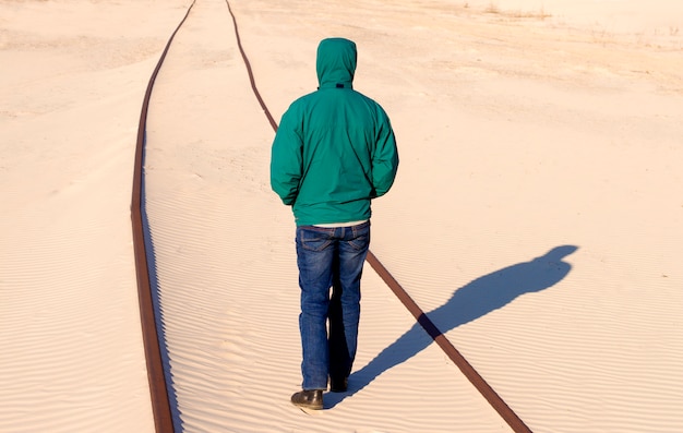 El hombre se para en el ferrocarril en la arena