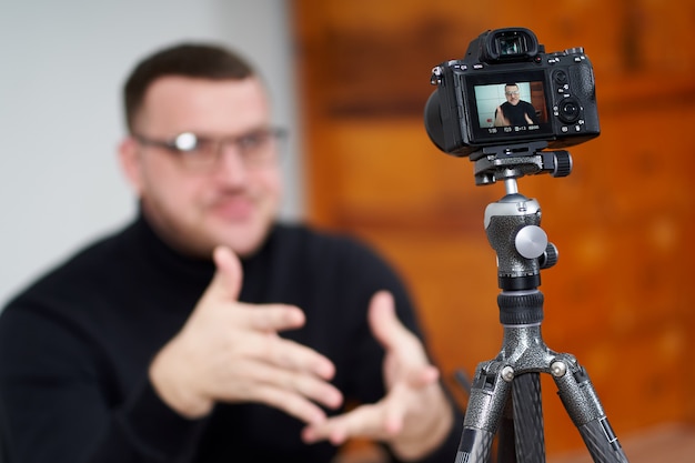 Hombre filmando video blog en cámara con trípode para seguidores en línea. En redes sociales, Influencer, nuevas tecnologías y concepto de internet.