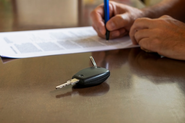 Hombre firmando un coche de alquiler o un documento de seguro en papel. Firma escrita en contrato o convenio.