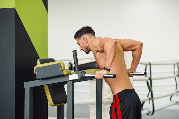 Hombre de fitness deportivo haciendo flexiones en barras paralelas mientras entrena en el gimnasio moderno. Concepto saludable y deportivo.